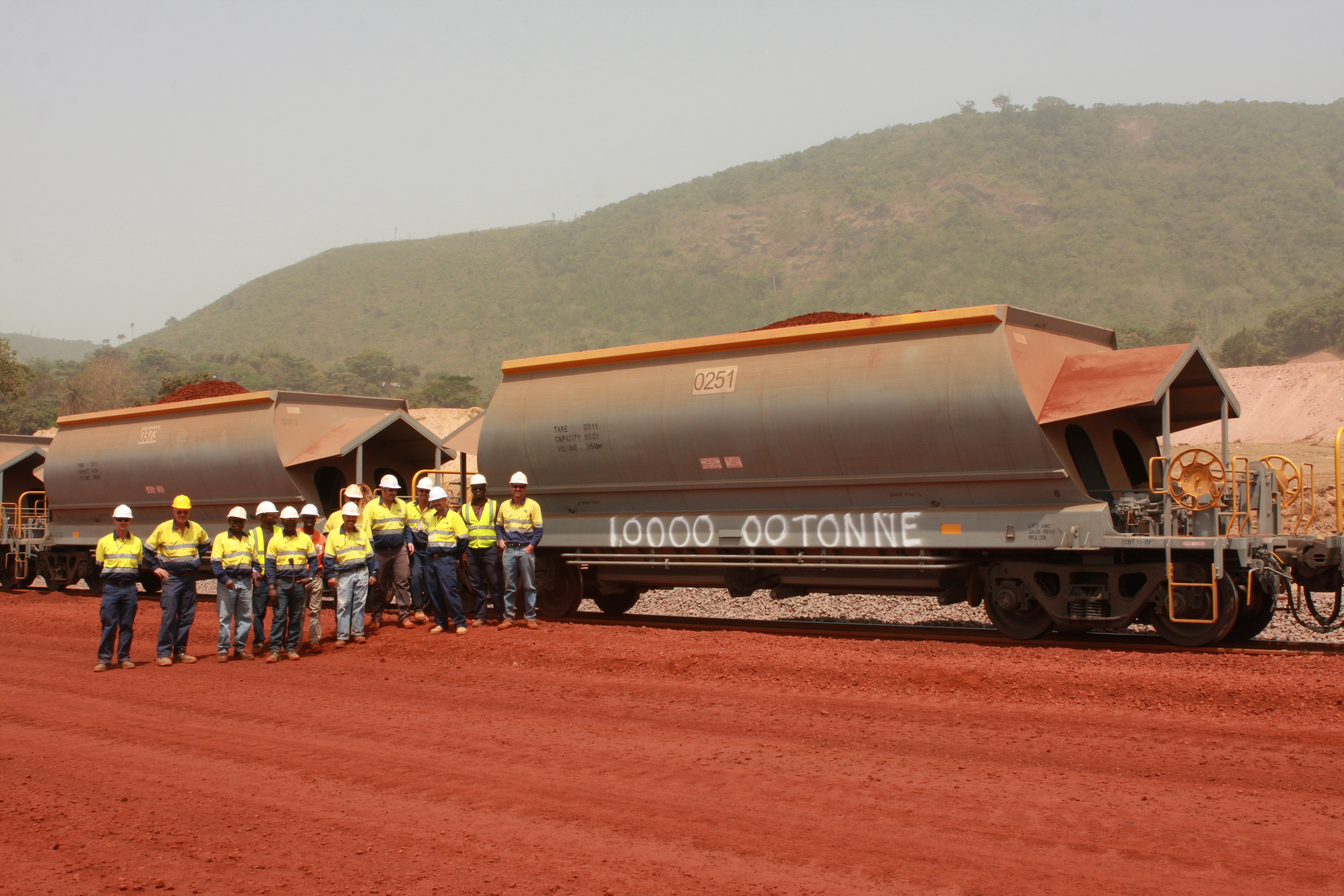 Mine crew in high-visibility gear beside a large iron-ore rail hauler