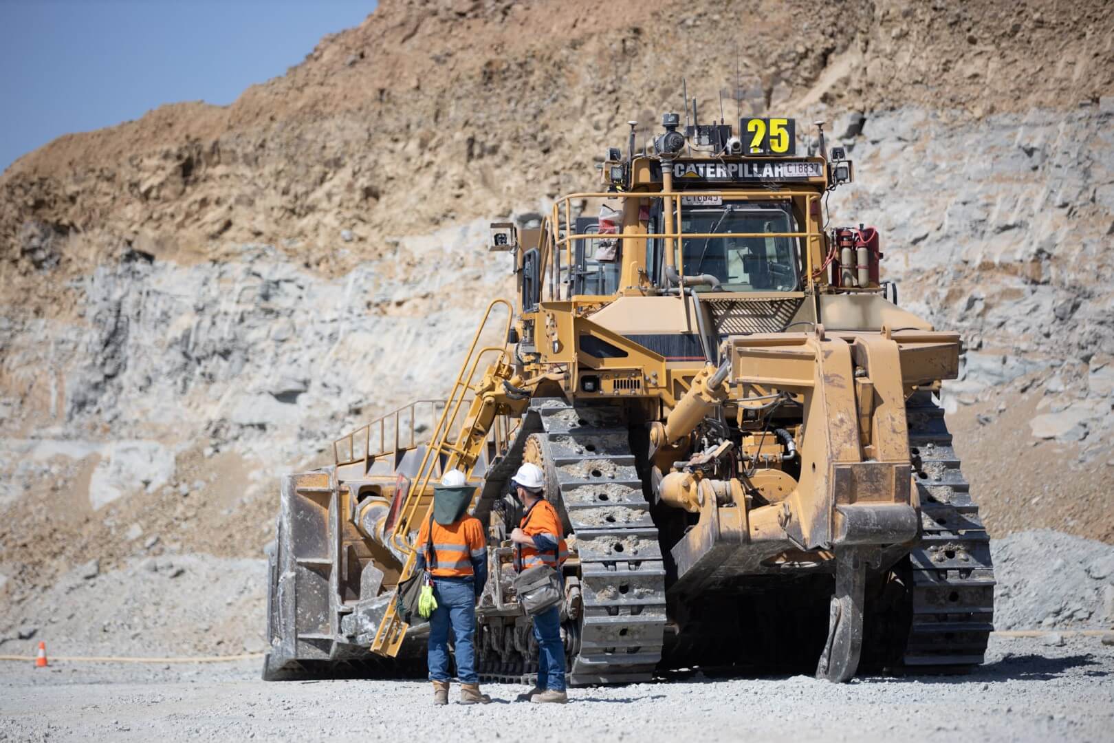 Two workers beside a large Caterpillar dozer at an open-pit mine