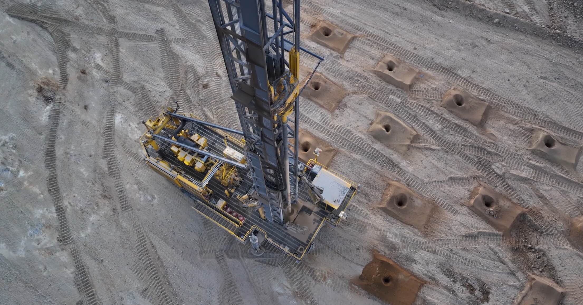 Aerial view of a drill rig drilling a blast-hole pattern in an open-pit mine