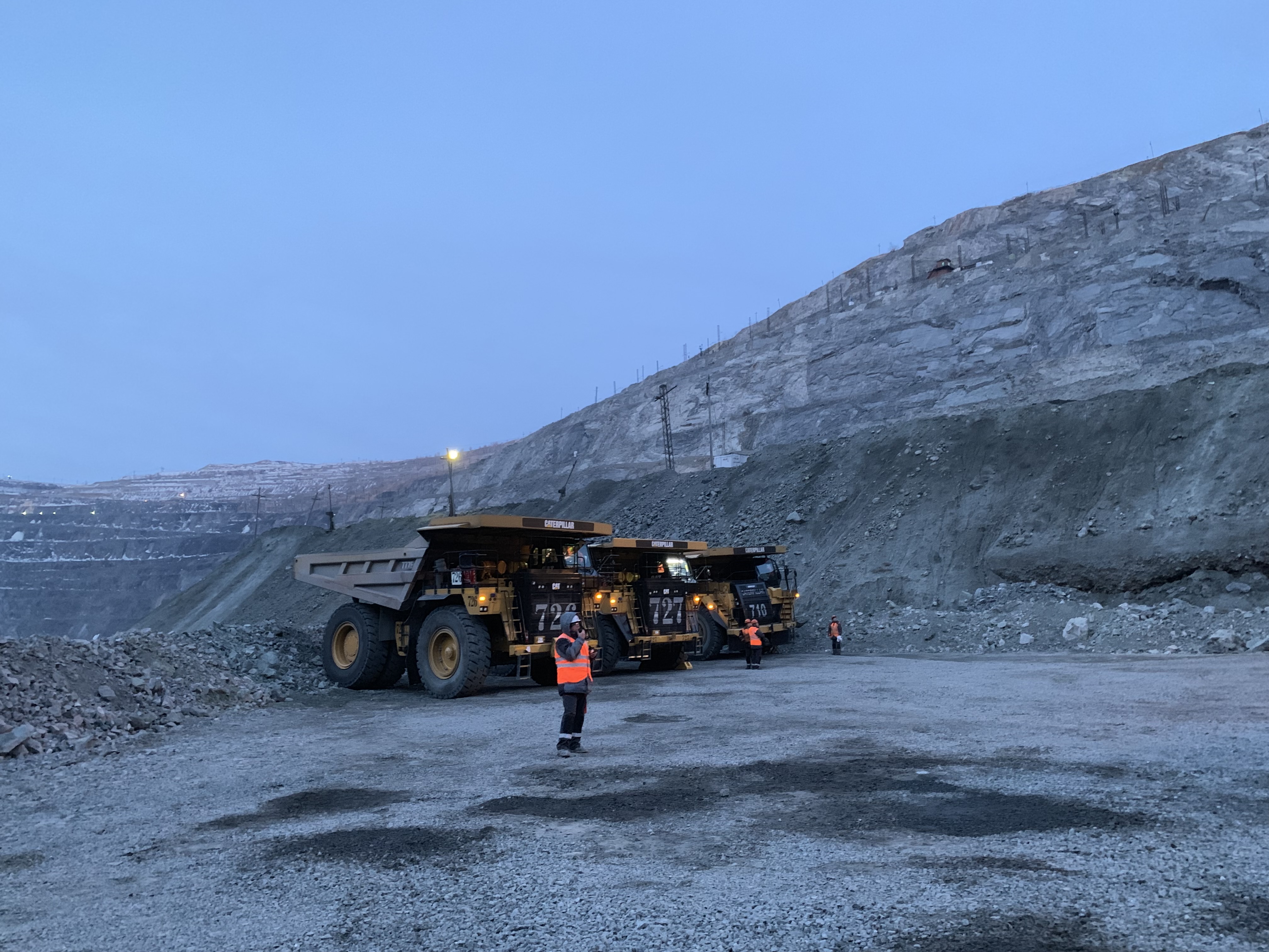 Worker standing beside a haul truck in an open-pit mine at dusk
