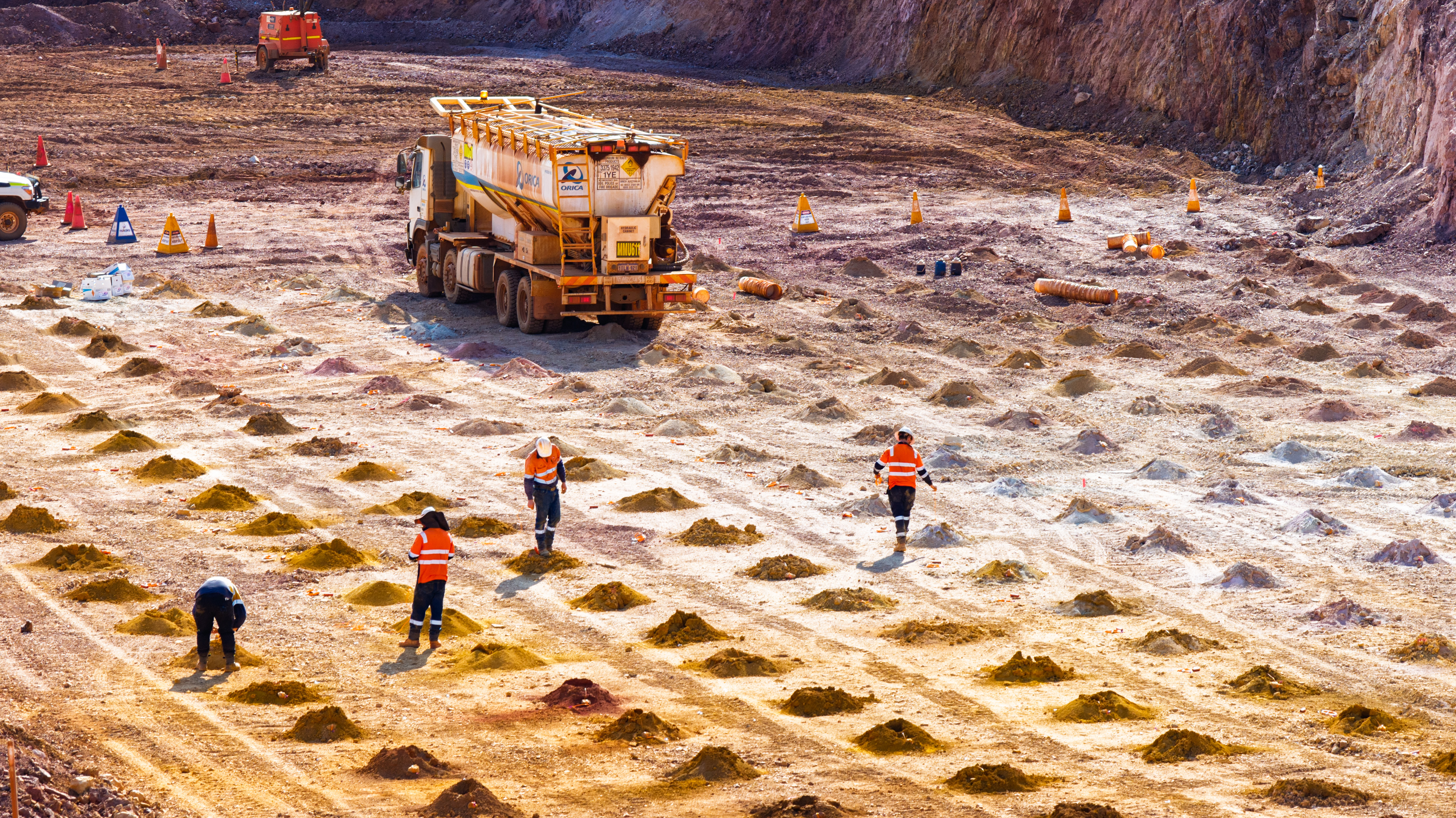 Shot crew loading blastholes and tying in a blast pattern with a mobile processing unit (MPU) truck at an open pit