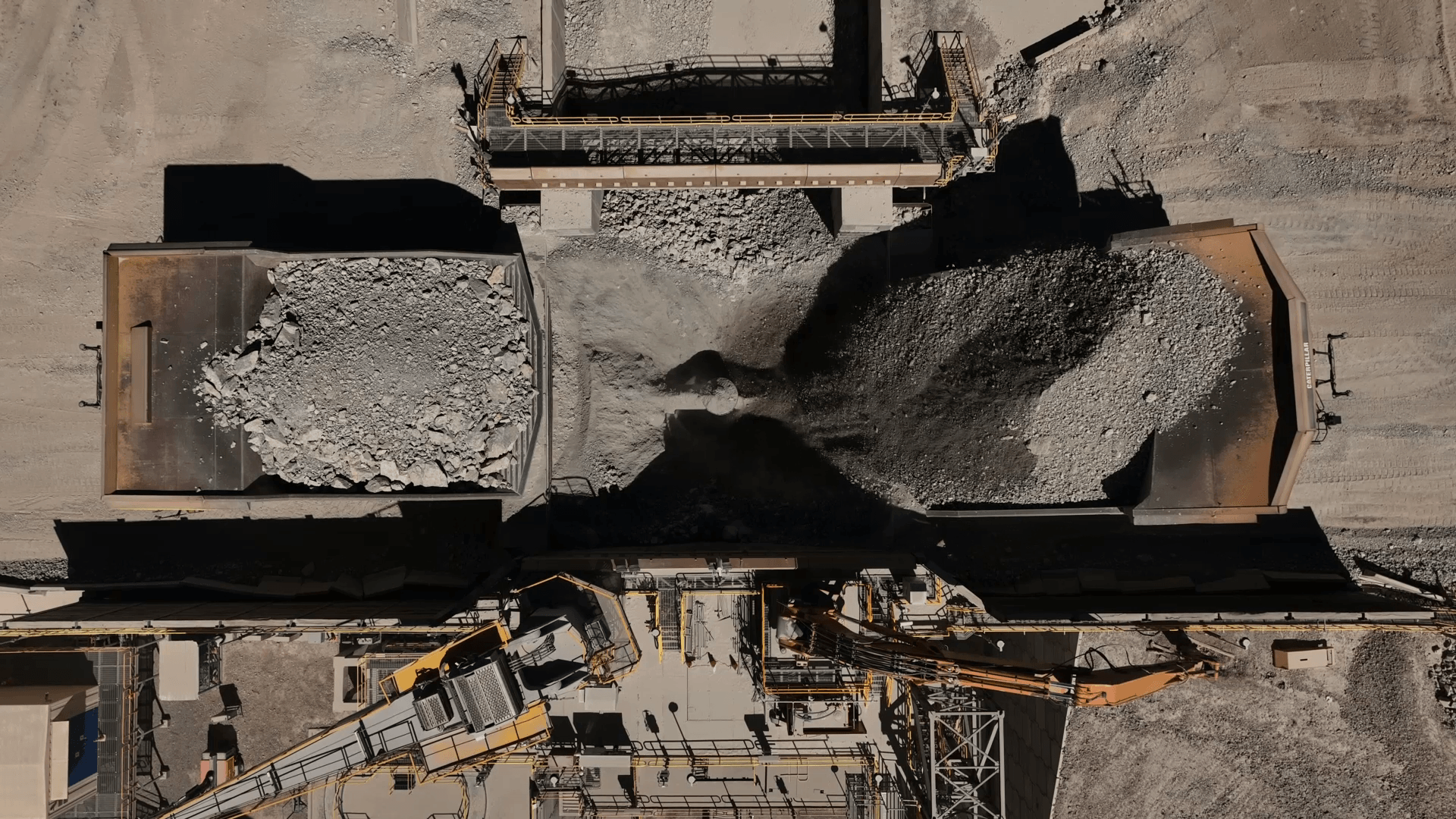Aerial view of two haul trucks direct tipping ore into a dual tip surge bin and gyratory crusher in Chile