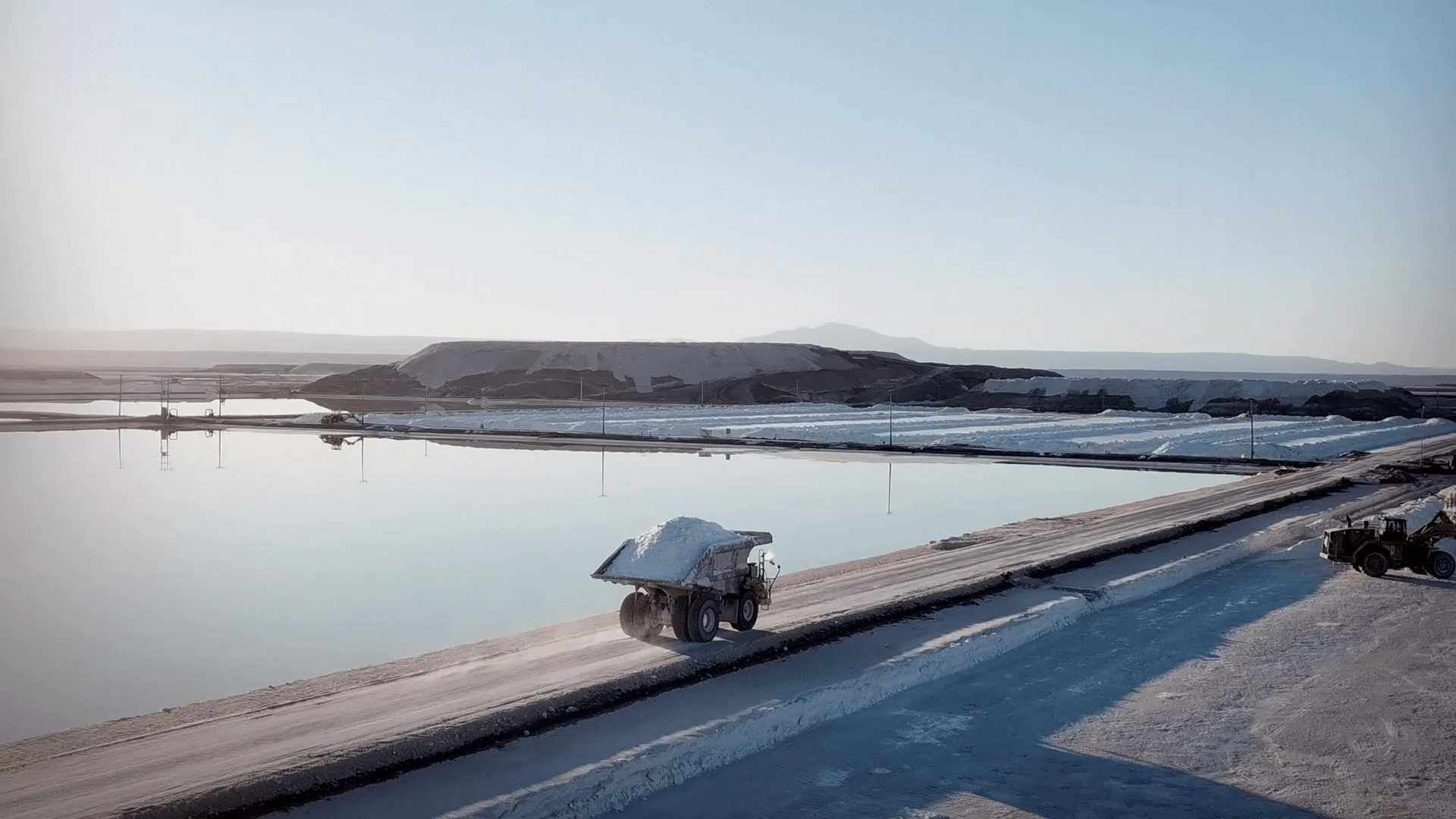 Dump truck hauling white salt along a haul road beside evaporation ponds at a salt mining operation