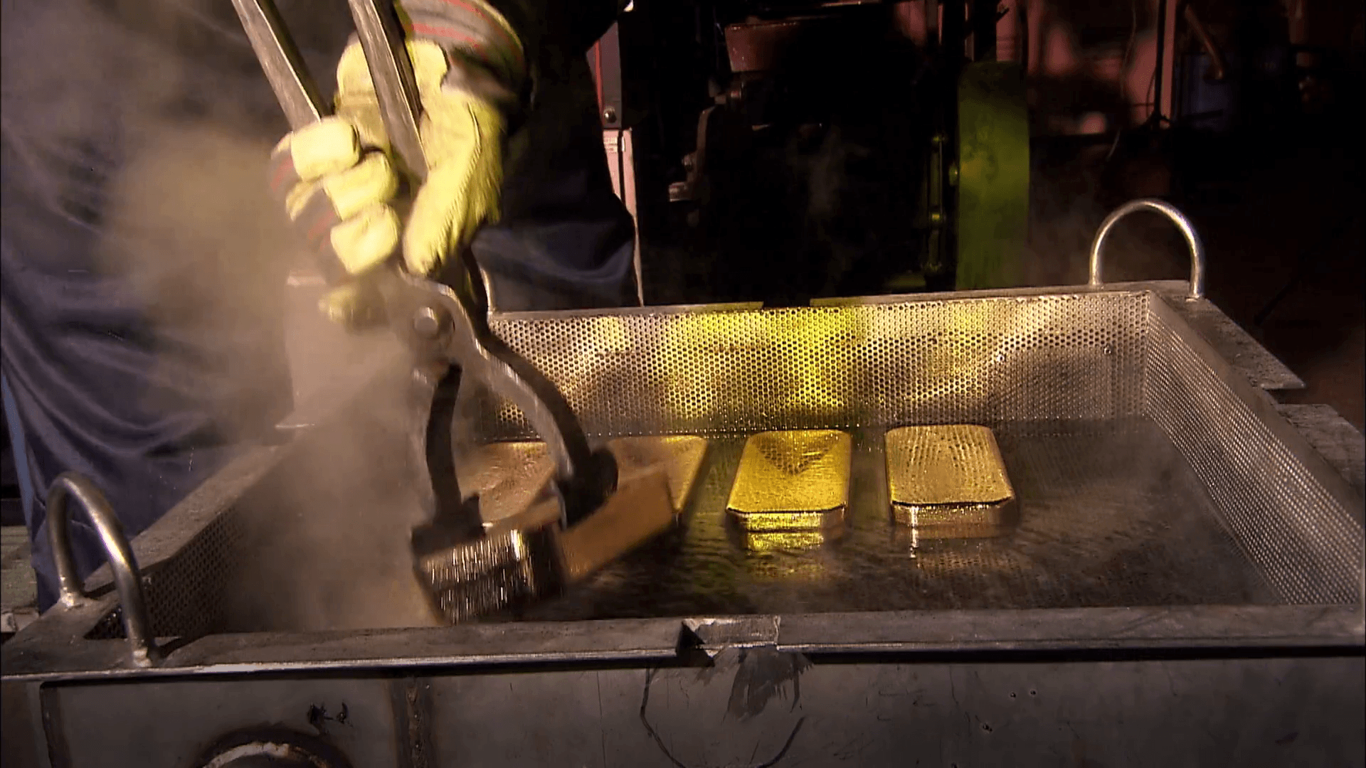 Worker using tongs to handle freshly poured gold doré bars in a quench tank during a gold pour